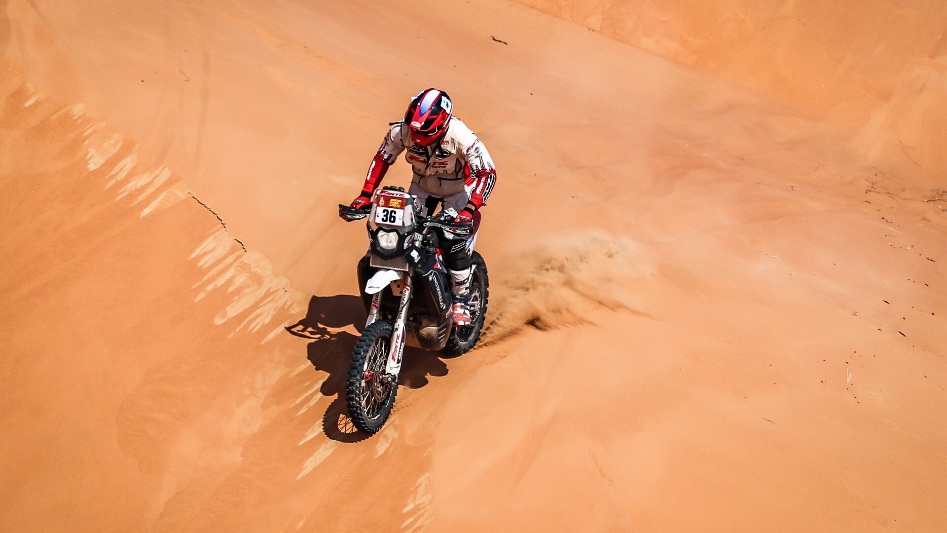 A Dakar rally rider crossing a steep orange sand dune